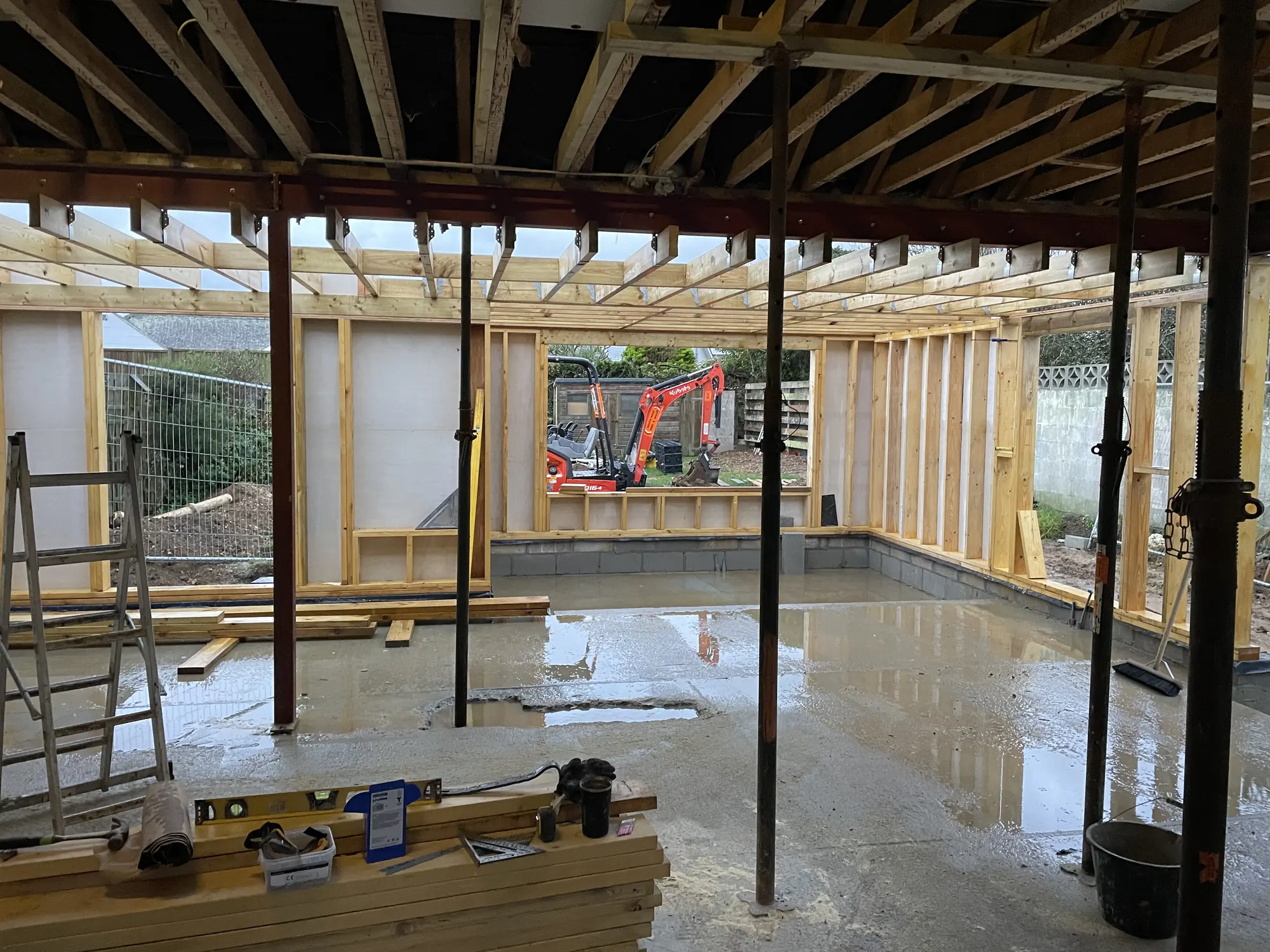 Timber-framed extension under construction with exposed steel beams, roof joists and support props